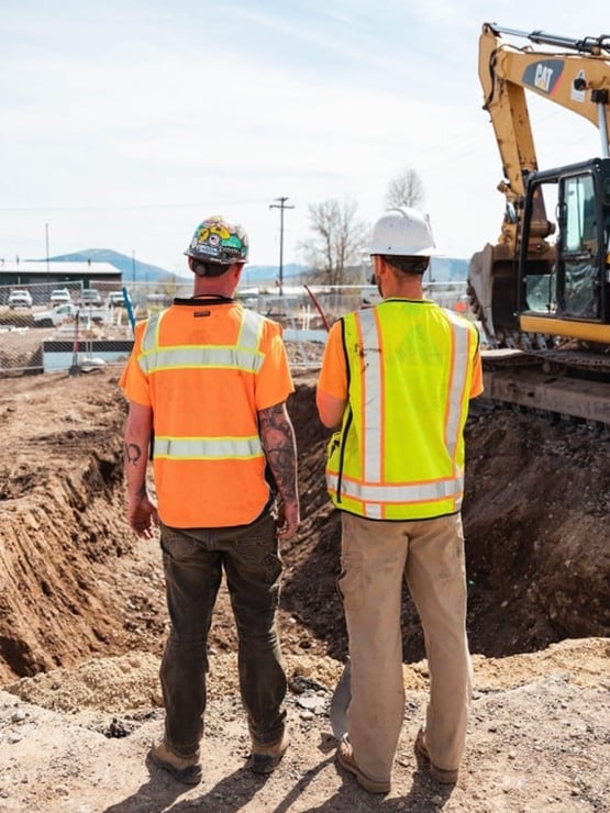 Two construction workers overlooking a work site with an excavator